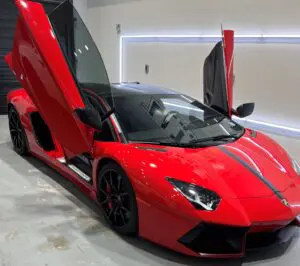 A red lamborghini parked in a garage with its doors open.